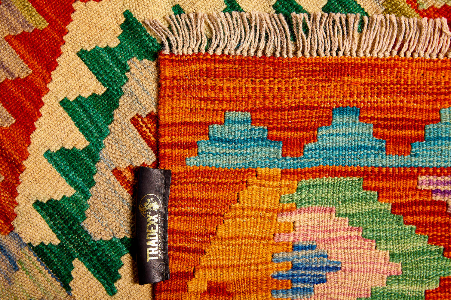 Close-up of a colorful patterned kilim rug with Tradexx - The Artisan Company brand tag visible
